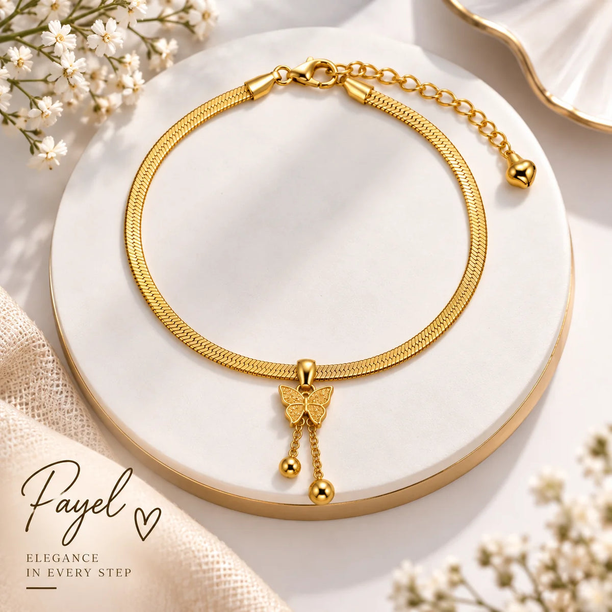 A gold snake-chain necklace with a butterfly charm and dangling gold beads, displayed on a round white marble stand with decorative flowers and fabric around it. The brand name 'Payel' is printed in the lower-left corner.