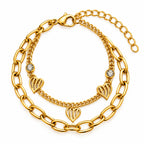 A gold-toned multi-strand bracelet featuring a chunky link chain, a delicate chain, three heart-shaped charms, and two bezel-set clear rhinestones, displayed on a clean white background.