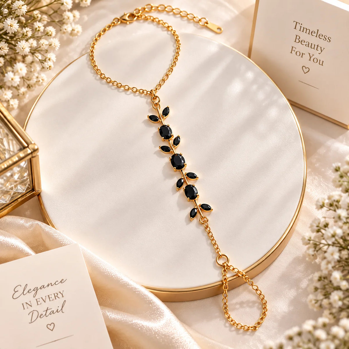A gold chain shoulder necklace with a leafy vine design set with dark blue gemstones, displayed on a round white tray with elegant props.