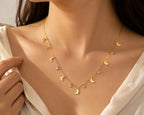 A close-up of a woman wearing a delicate gold necklace with multiple small crescent moon charms and tiny clear rhinestone accents, styled with a white blouse.