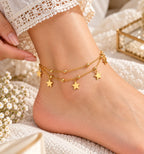 A close-up of a person's ankle and foot wearing a delicate gold double-layer anklet with star charms, styled with lace-trimmed socks and small white flowers.