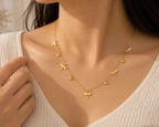 A close-up of a woman wearing a delicate gold necklace with five dragonfly charms and small clear stone accents, styled with a cream ribbed top.