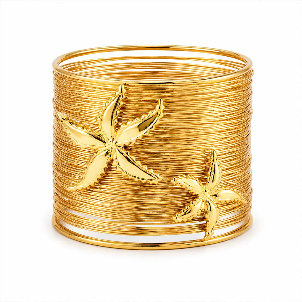 A wide gold bangle cuff made of tightly wrapped metallic bands, decorated with two raised starfish motifs, shown on a plain white background.