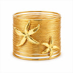 A wide gold bangle cuff made of tightly wrapped metallic bands, decorated with two raised starfish motifs, shown on a plain white background.
