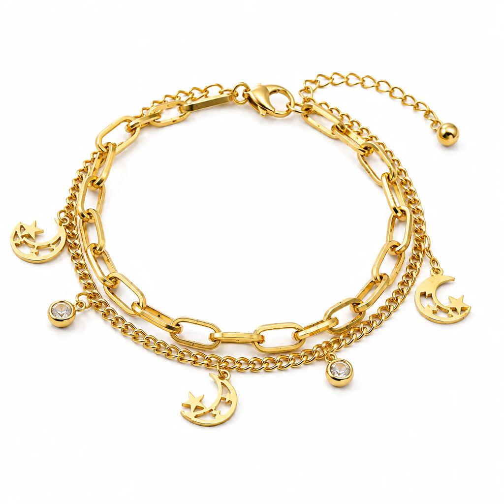 A gold-toned multi-layer bracelet featuring a combination of paperclip and curb chains with dangling crescent moon and star charms, along with two small clear crystal charms, shown on a plain white background.