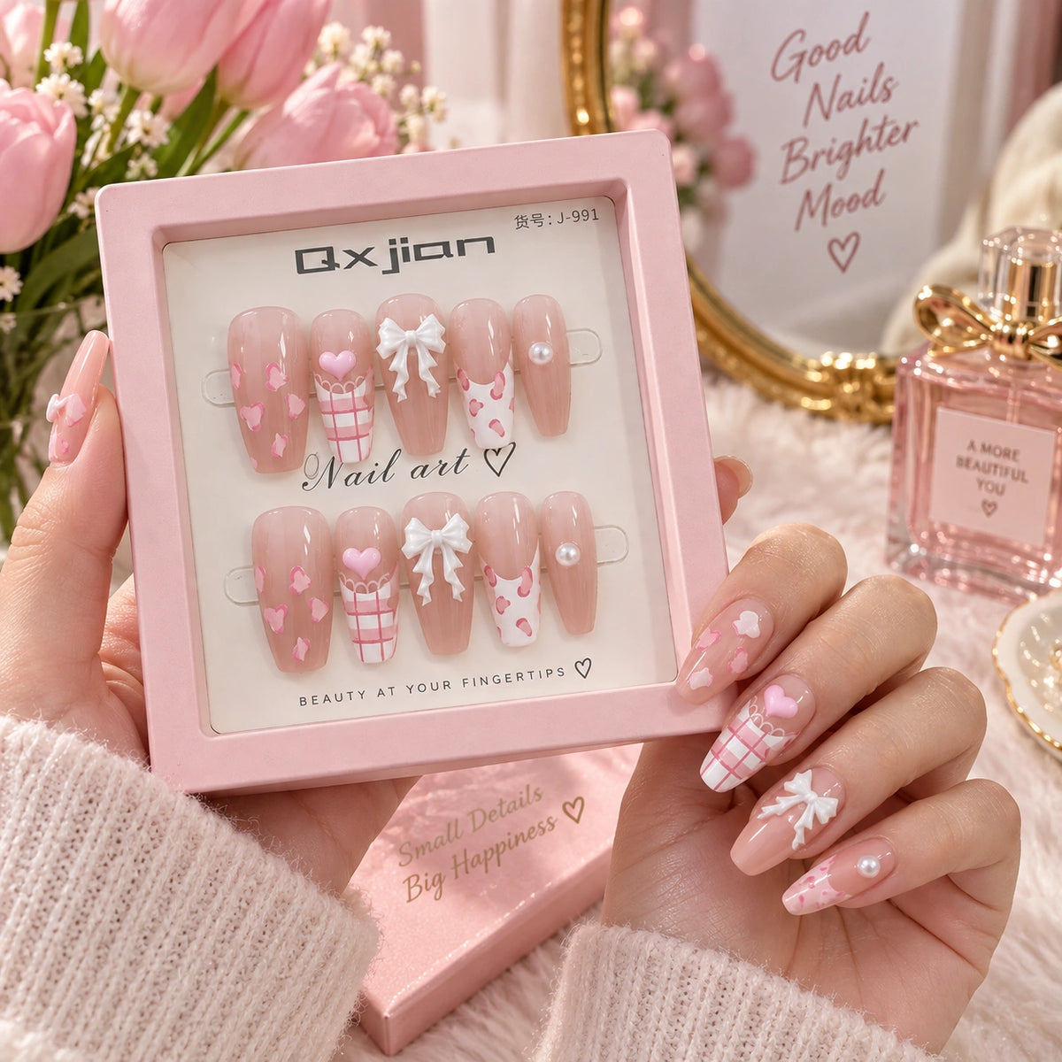 A person holds a pink box of false press-on nails. The nails have a pale pink nude base with white hearts, plaid patterns, and white bows.
