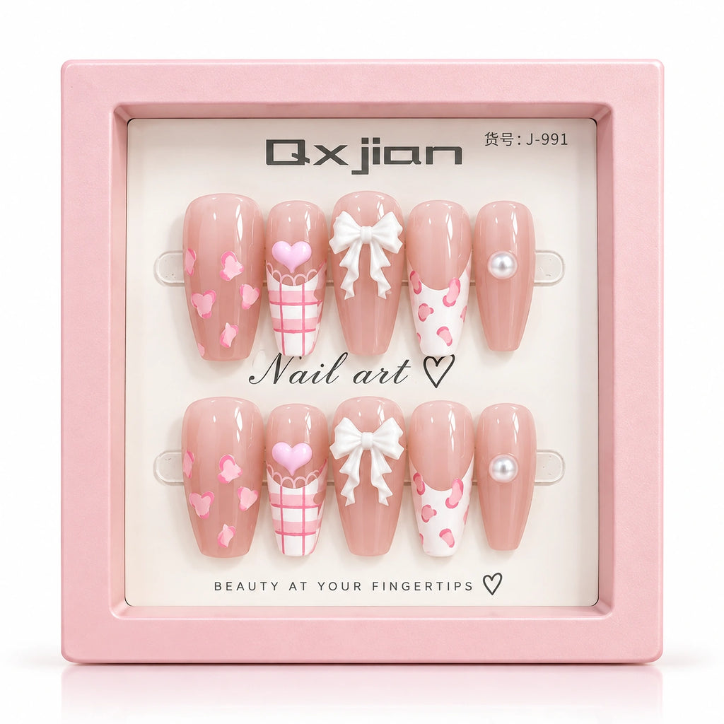 A pair of pink press-on nails displayed in a square pink box. The nails have a glossy nude-pink base with white bows, pink hearts, pink plaid patterns, and pearl accents.
