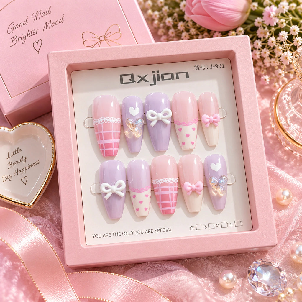 A boxed set of false press-on nails in pastel pink, lavender, and cream tones, arranged in a pink presentation tray with the brand name 'Ox jian' visible on the insert. The set includes bows, hearts, stripes, and small decorative embellishments.