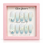 A set of 10 press-on nails displayed in a pink presentation box. The nails feature a light blue to white gradient with white bows, rhinestones, and delicate floral designs.