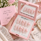 A hand holds an open pink press-on nail kit showing 10 decorated pink nails with white lace and bow designs. The kit includes a mirror on the inside lid, a pink box labeled 'Good Nails Brighter Mood,' and a card reading 'A Brighter You.