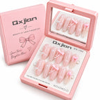 Pink press-on nail set with bow and floral designs, shown in an open pink case with a mirror, alongside the matching pink Qxjian box.